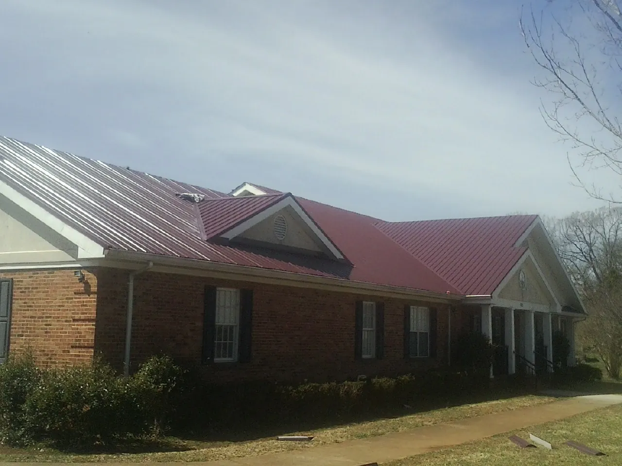 Red metal roof with gabled entries on a long brick building, from a Hail Damage Roof Repair job in Livingston Manor
