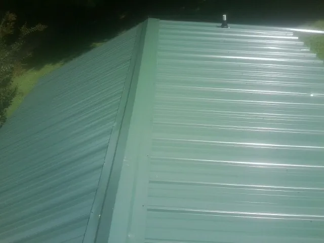 New green metal panels meeting at the ridge of a roof — Flat Roof Repair work by our crew in Livingston Manor