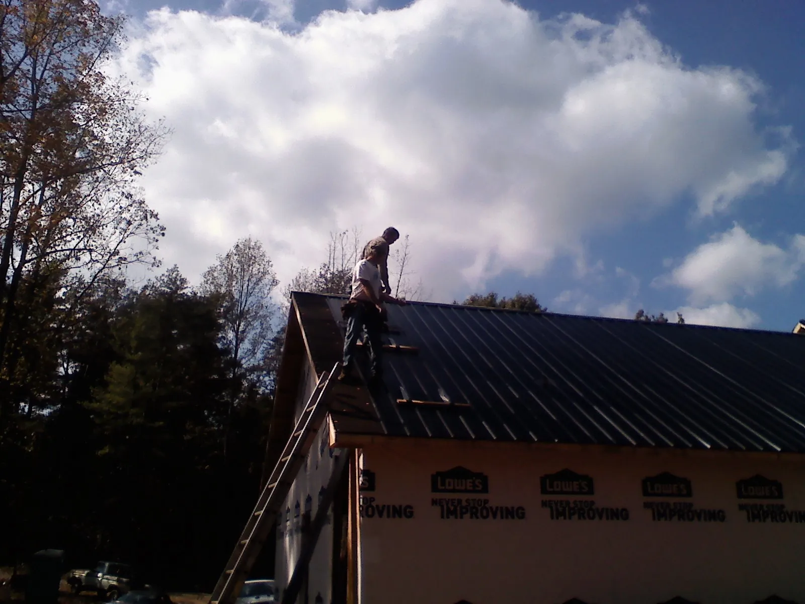 Roofer fastening dark metal panels high against a cloudy sky, from a Roof Inspection job in Livingston Manor