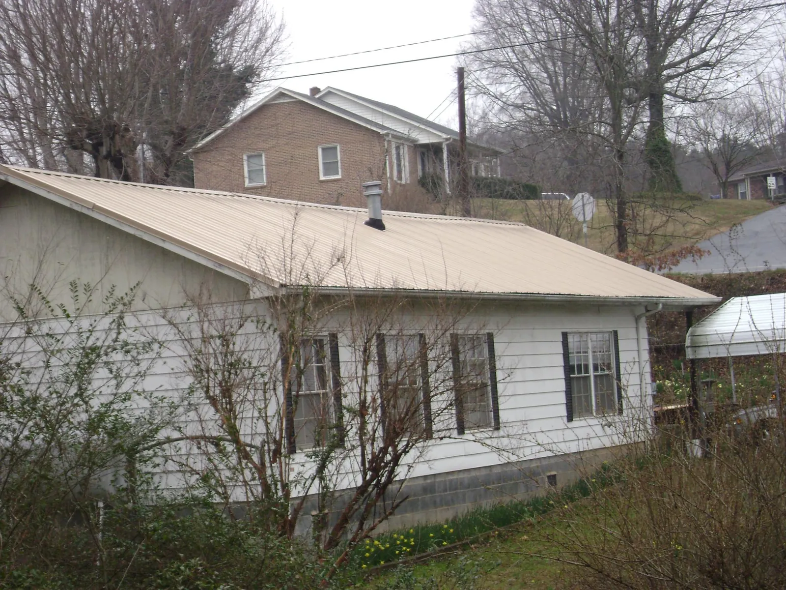 Tan metal roof on a white sided house set into a hillside — Commercial Roofing by Roofing Brothers in Livingston Manor